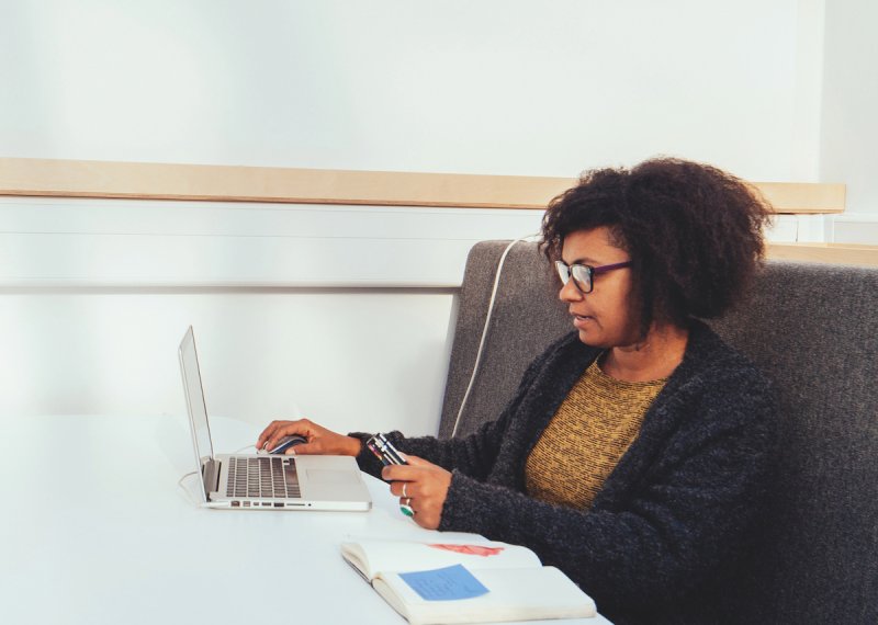 Female student seated at white table with laptop and open notepad