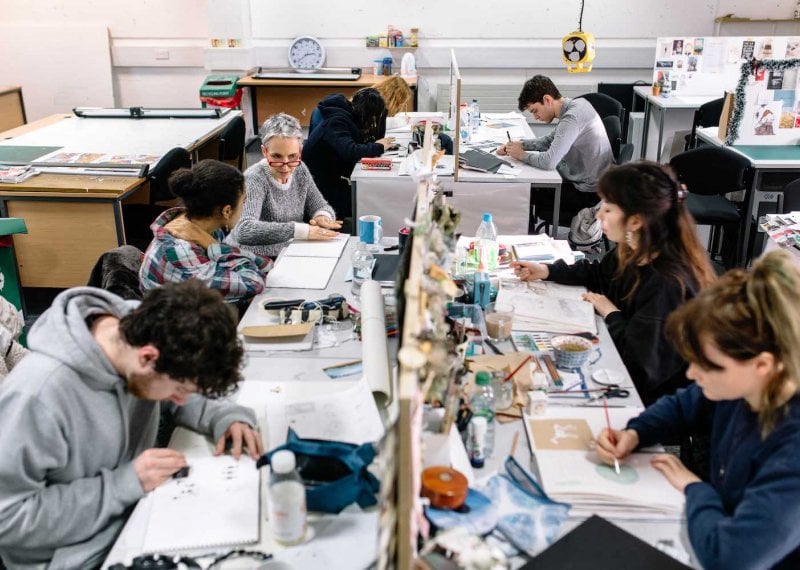 Illustration students in busy studio at desks drawing.