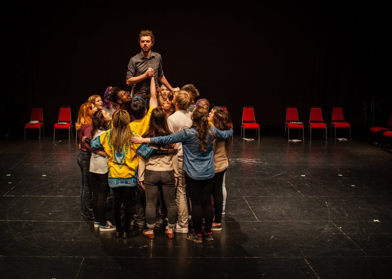 A group of acting students in a huddle with a male actor standing above them