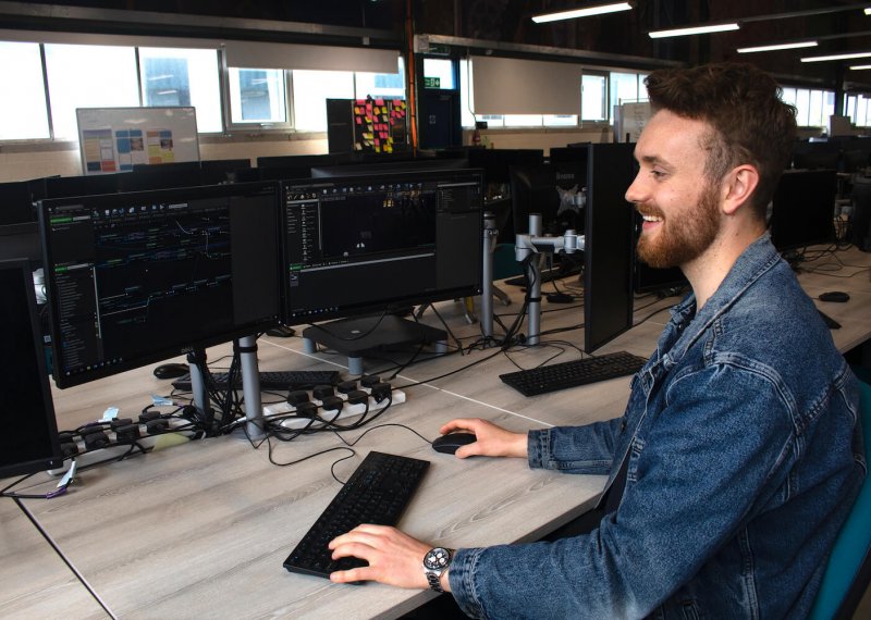 A Falmouth University Games student smiling at a computer screen with a keyboard and mouse