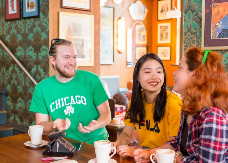 Three students at table coffee shop laughing.