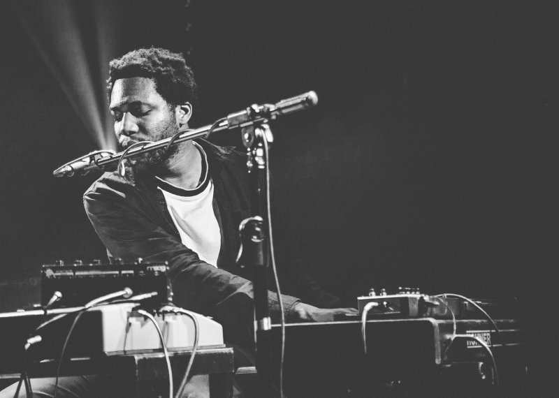 Grayscale image of student singing into microphone and playing keyboard.