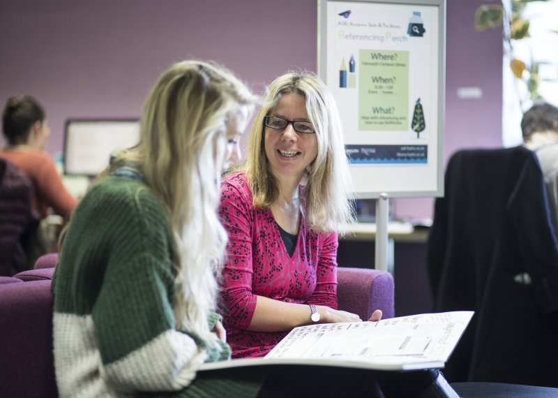 Member of staff chatting with student in library.