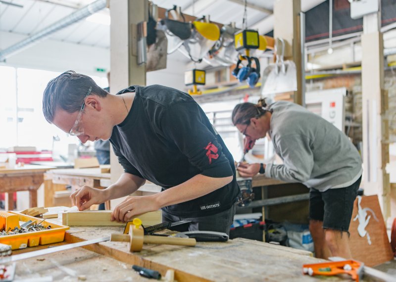 Male students wearing goggles working in a wood making workshop