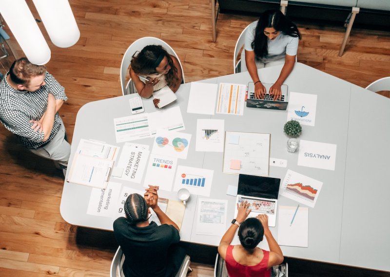 Birds eye view of group of people sat around a table with business strategy papers