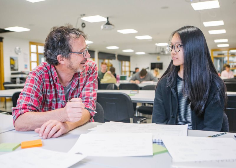 a male staff member talking to a female student at a desk