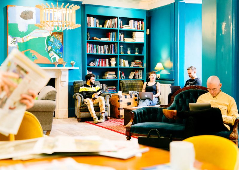 A group of students seated on sofas in a blue room with book cases and art on walls