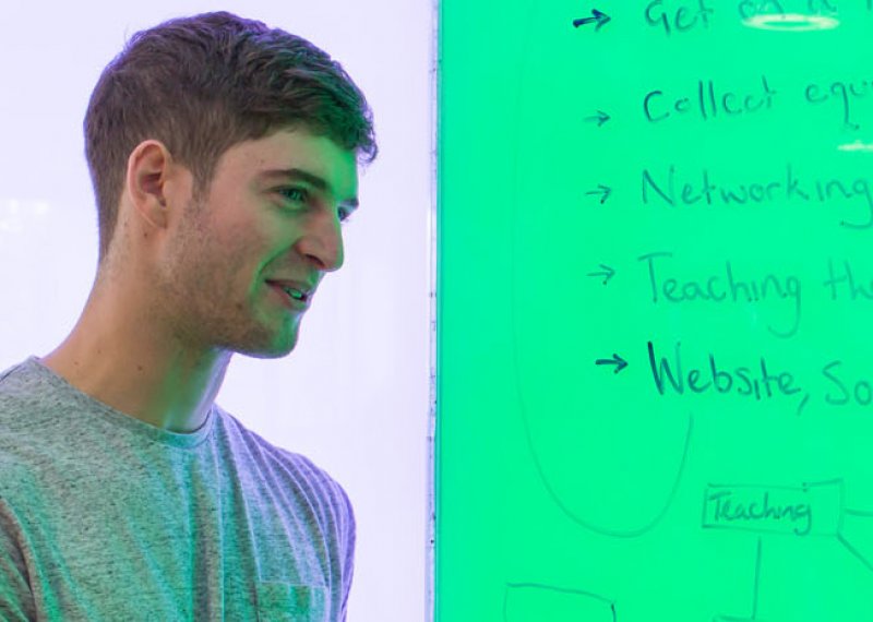 A Falmouth University male student writing on a green board