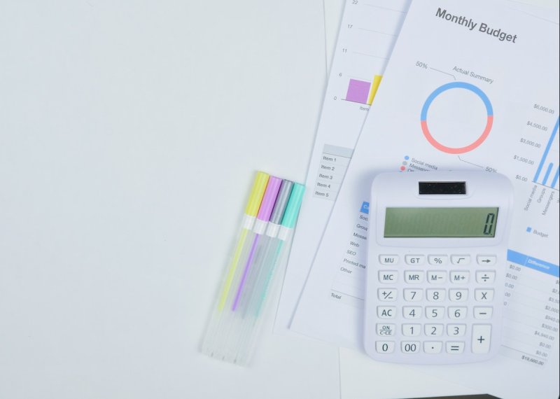 A white calculator and pens next to paper with financial graphs