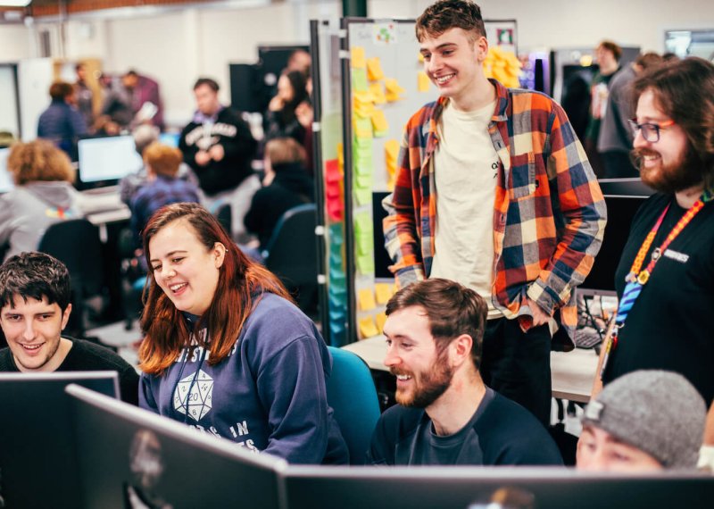 A group of games students smiling and laughing around a computer