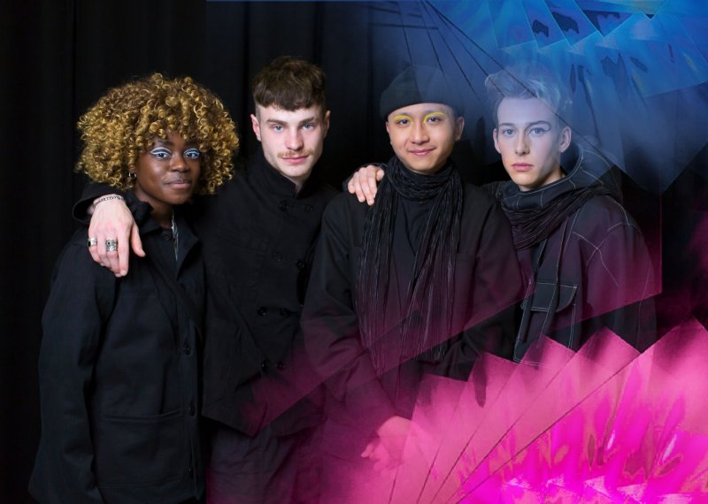 Four students standing together and looking into the camera wearing black garments designs by a student.