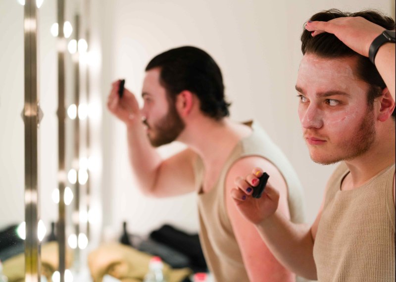 Two men look into mirrors, doing their makeup before a performance