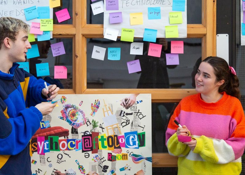 Two students talking in front of a wall with post-it notes