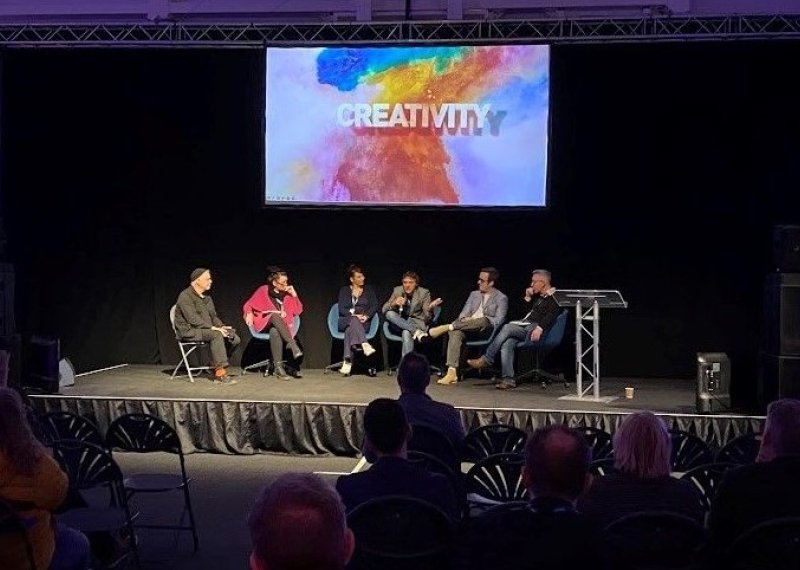 Six people sitting in chairs on a stage with a screen behind them