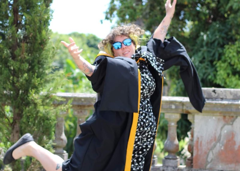 A woman wearing a graduation gown leaps into the air