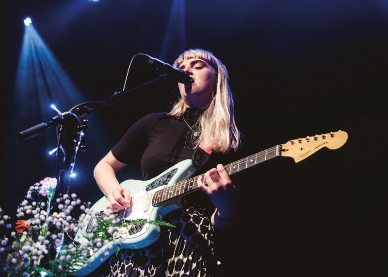 Student singing into microphone on stage and playing guitar