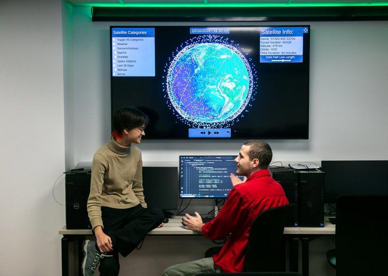 Two software engineering students in discussing with large screen of the world on the wall