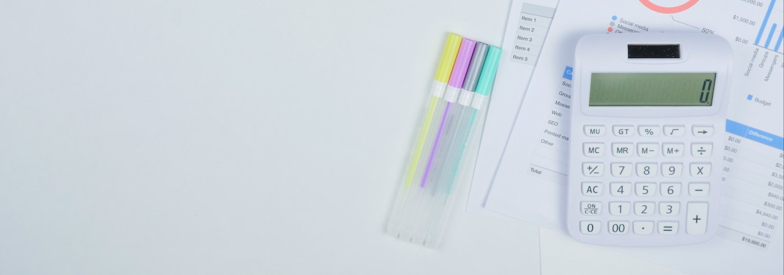 A white calculator and pens next to paper with financial graphs