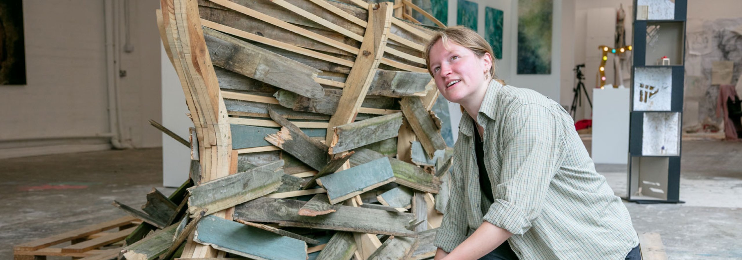 A Fine Art student kneeling by her wooden boat installation