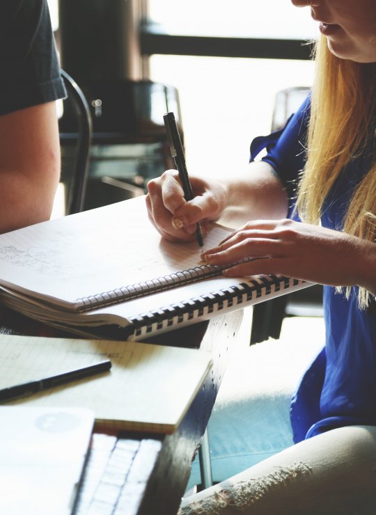 Business students sat around a desk, taking notes and drinking coffee.