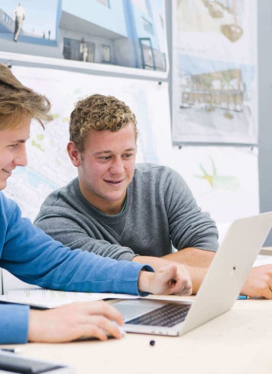 Two male students seated while looking at a laptop