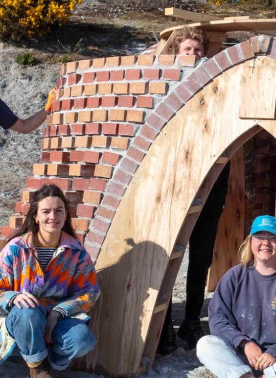 Architecture students outside a brick building with wooden arch