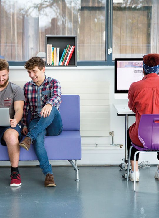 Three business management students working at a laptop and desktop