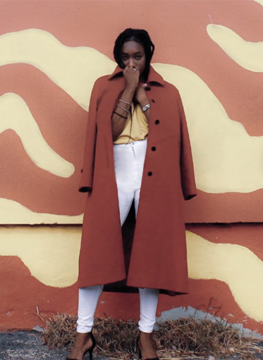 A woman in a red coat in front of a yellow and red wall