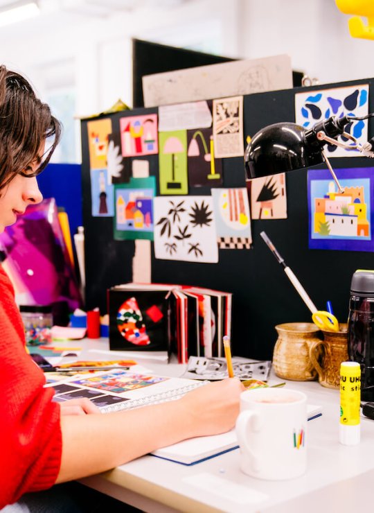 Falmouth University Illustration student wearing a red jumper and drawing at a desk