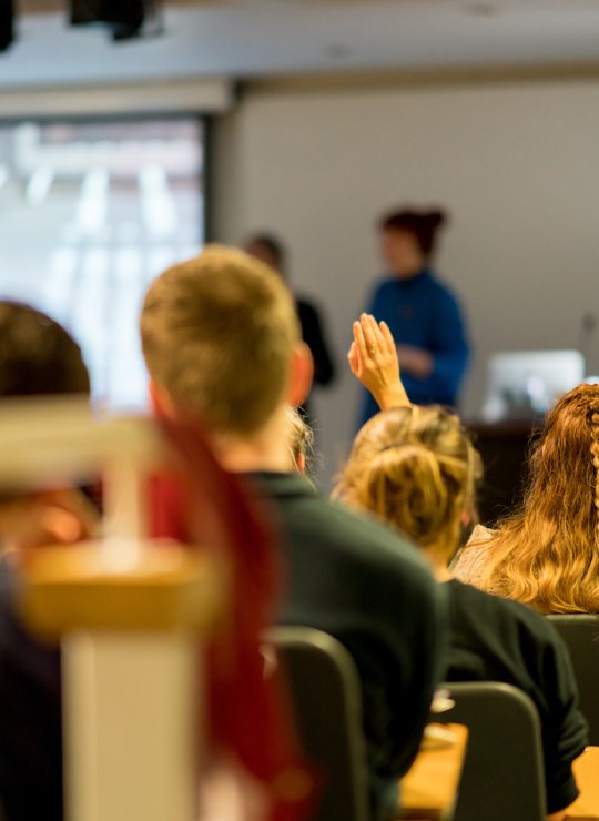 A lecture theatre with students raising their hands