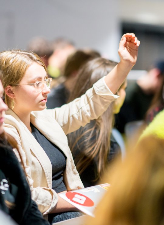 Female student raising hand in a crowd
