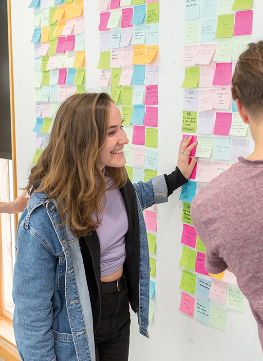 People standing by board with ideas pinned to it