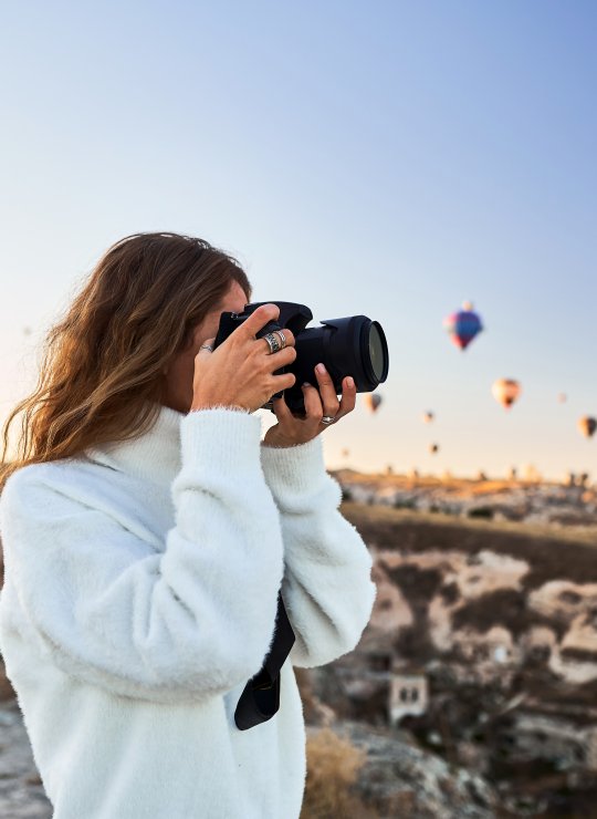 A student taking a photo standing underneath a sky full of hot air balloons