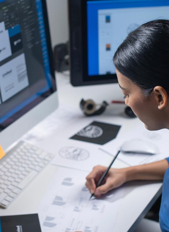 A woman drawing logos at a desktop computer