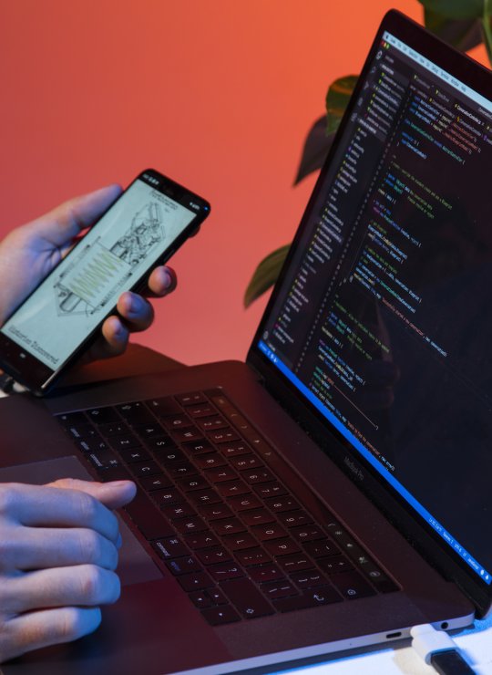 A laptop with code on the screen is connected to a phone with an app open.