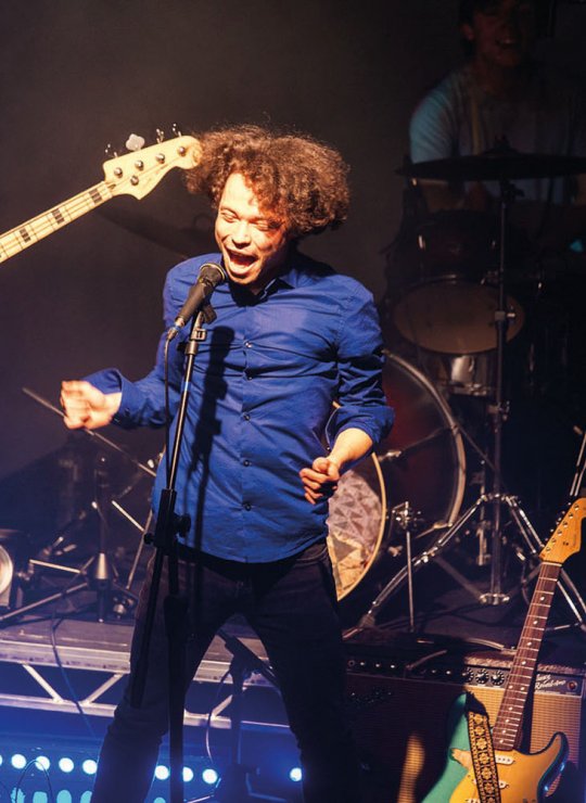 Student singing and jumping on stage in front of guitarist