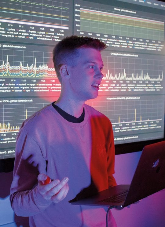 Student stood in front of large screen with code and graphs on