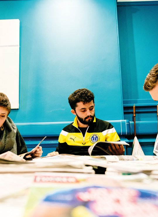 Students reading newspapers around a desk