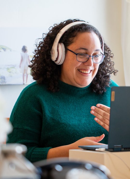 A woman wearing headphones smiling into her computer screen