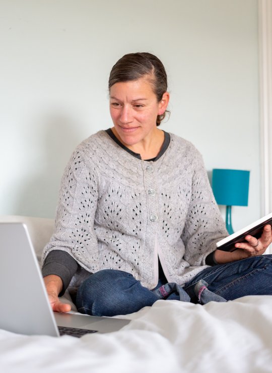 A woman sat in a bed working on her laptop