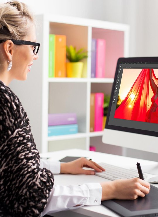 A woman working on an iMac editing a photograph of a woman in a red shawl