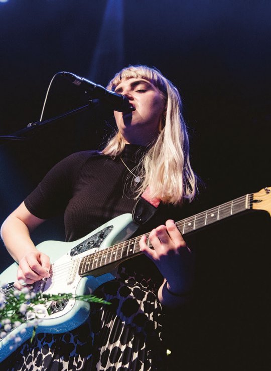 Student singing into microphone on stage and playing guitar