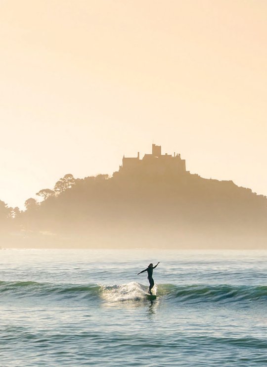 Surfer riding wave in front of St Michaels Mount