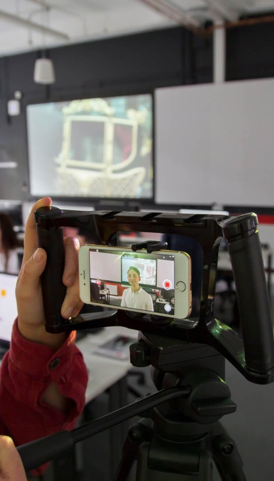 Student filming in the newsroom on a smartphone.