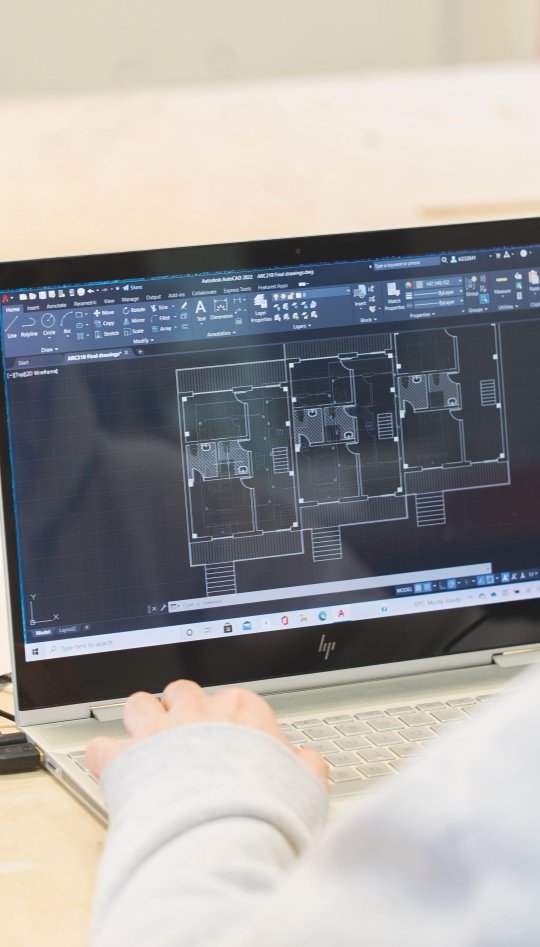Student at a laptop looking at blueprints