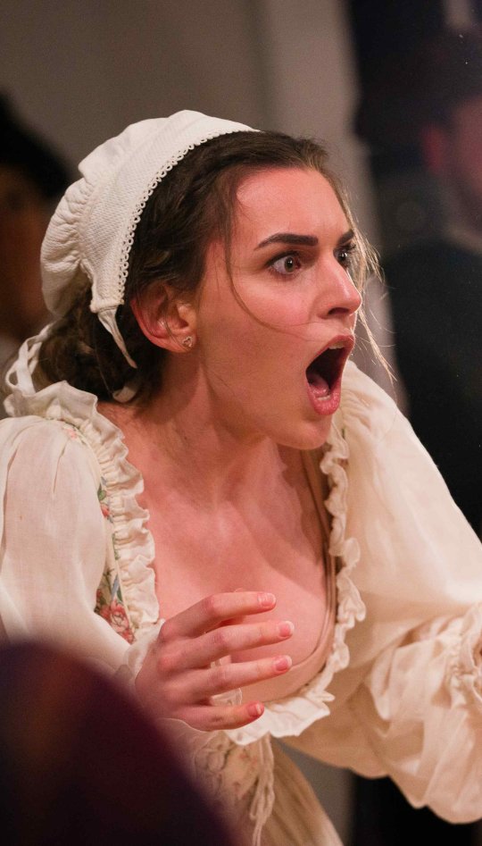 A woman dressed as a maid has a shocked expression on her face