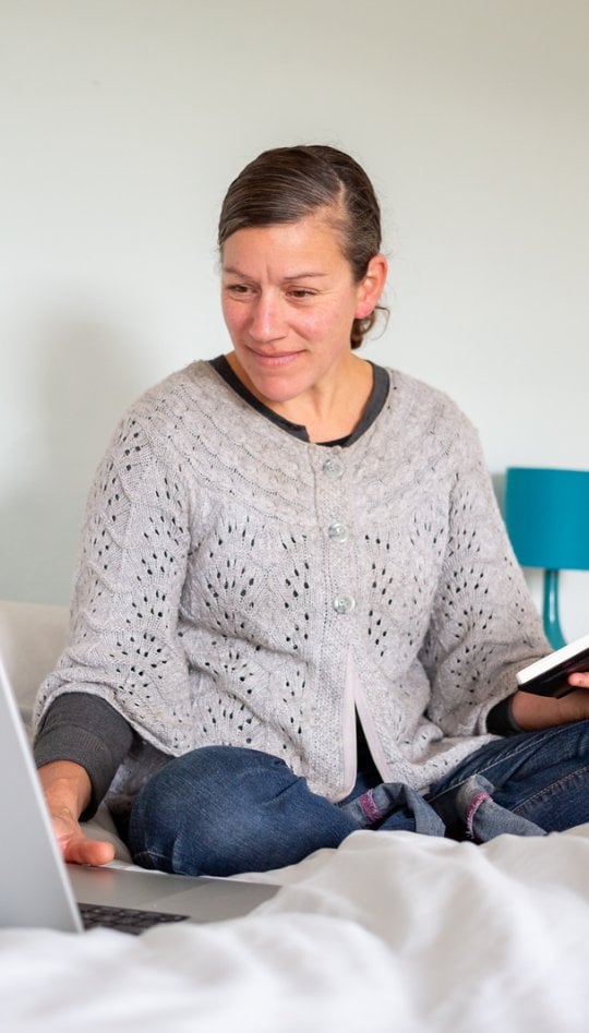 A woman sat in a bed working on her laptop