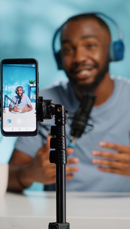 A man wearing headphones filming himself with his phone on a tripod