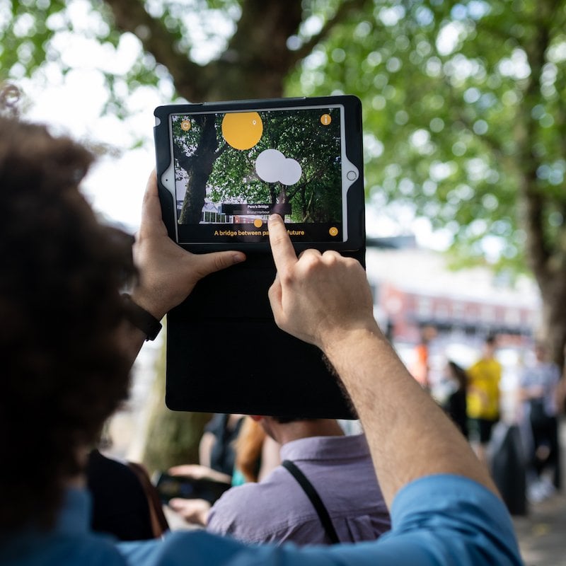 A man holding up an iPad in a street with trees