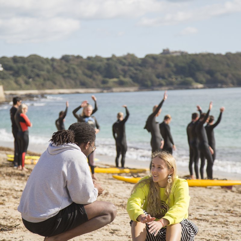 Two students talking on the beach in front of a surf lesson